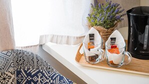 Une pièce accueillante avec une fenêtre, une machine à café, deux tasses en verre avec des sachets de thé, une petite plante en pot et un coussin à motifs.