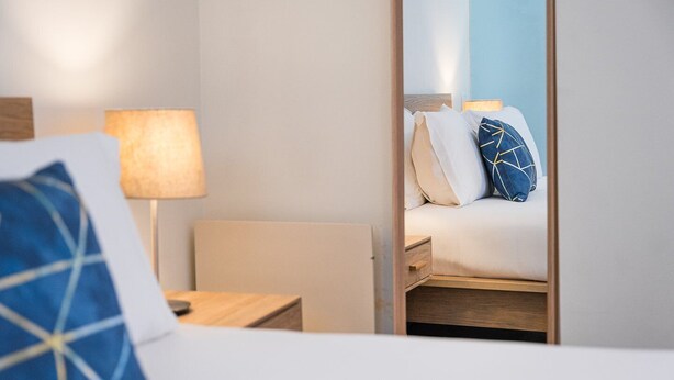 Une chambre d’hôtel avec un lit, une table de chevet, une lampe et un miroir qui reflète le lit et les oreillers.