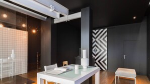 A modern meeting room with a glass table, white chairs, a wooden bench, and a black and white patterned wall. - GuestReady - Innvict Astern (Porto)