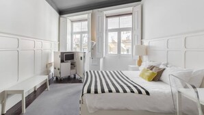 A hotel room with a bed, bedside tables, a TV, and a window with a view of buildings. - GuestReady - Innvict Astern (Porto)