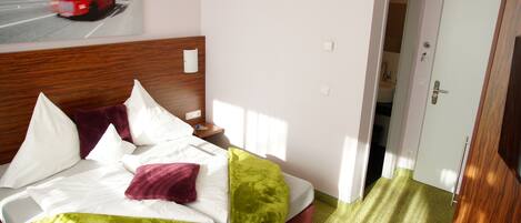 Una habitación de hotel con una cama, una mesita de noche, un cuadro de un autobús rojo de dos pisos y una puerta que da a un baño.