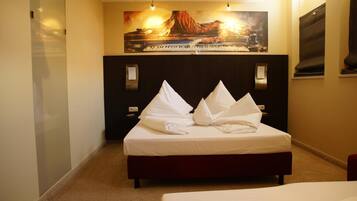 A hotel room with a bed, a nightstand, a wall-mounted lamp, and a painting above the bed.