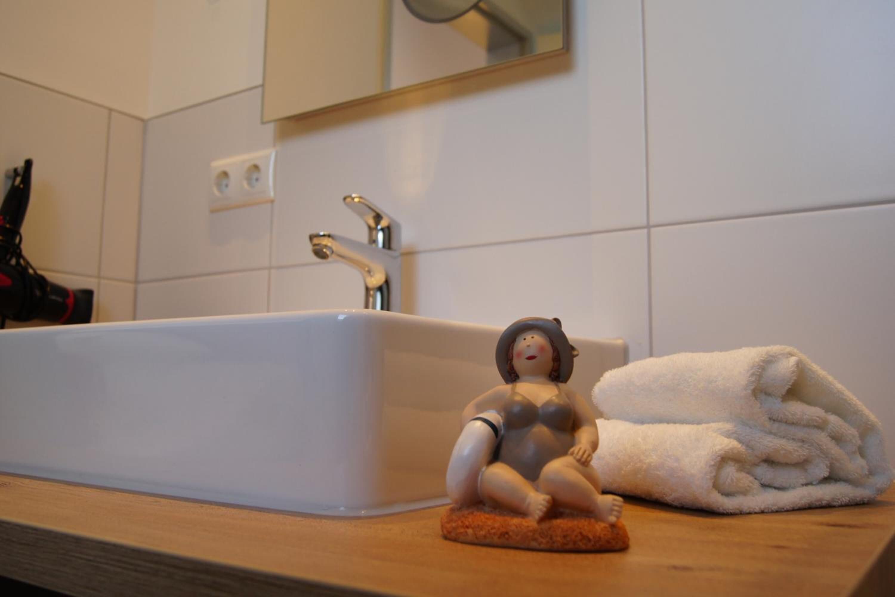 Ein Badezimmer mit einem weißen Waschbecken, einem Spiegel darüber und einer kleinen Figur auf einer Seifenschale.