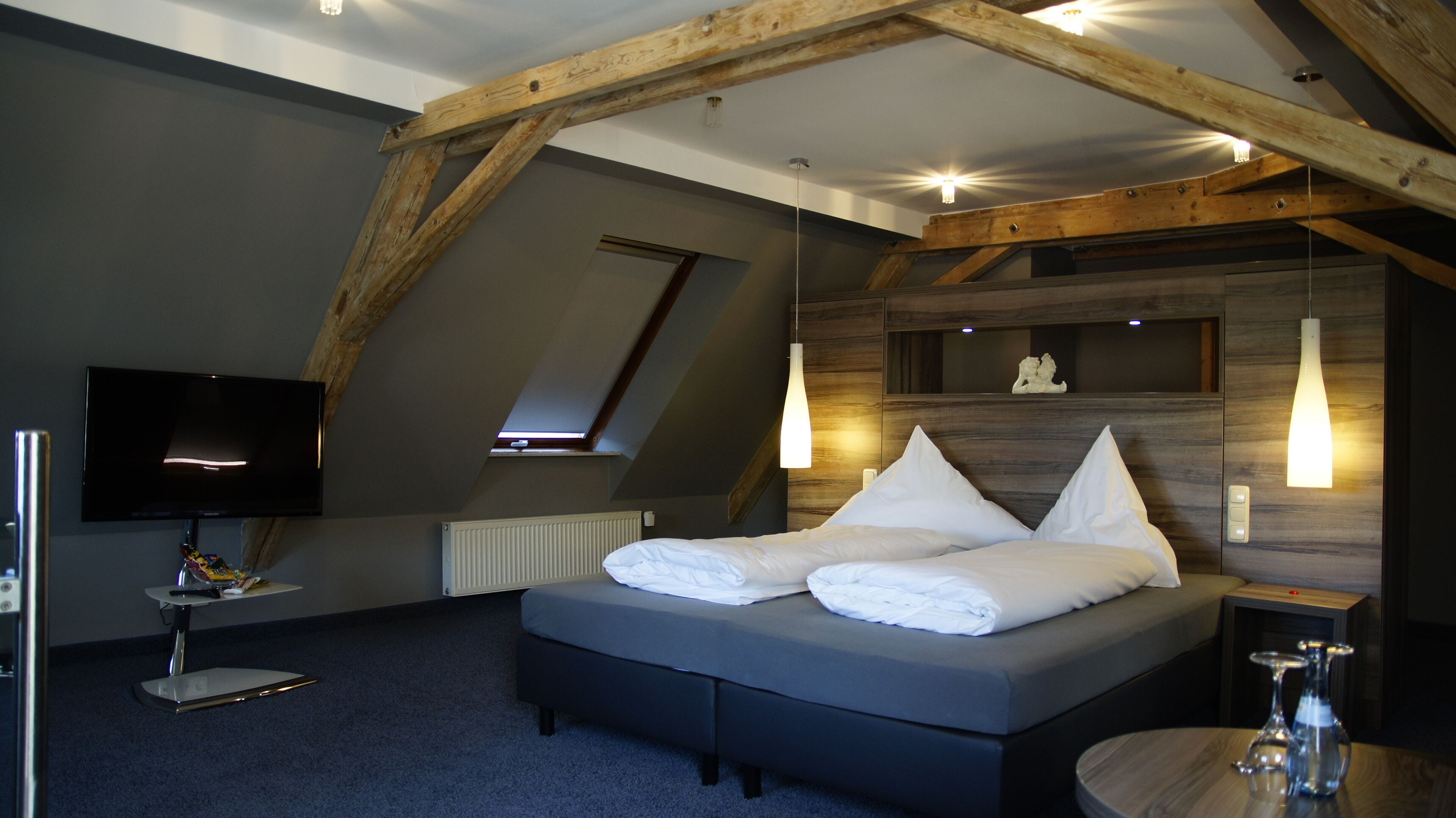 Un dormitorio moderno con techo inclinado, una cama grande, un televisor de pantalla plana y una mesita de noche con lámpara.