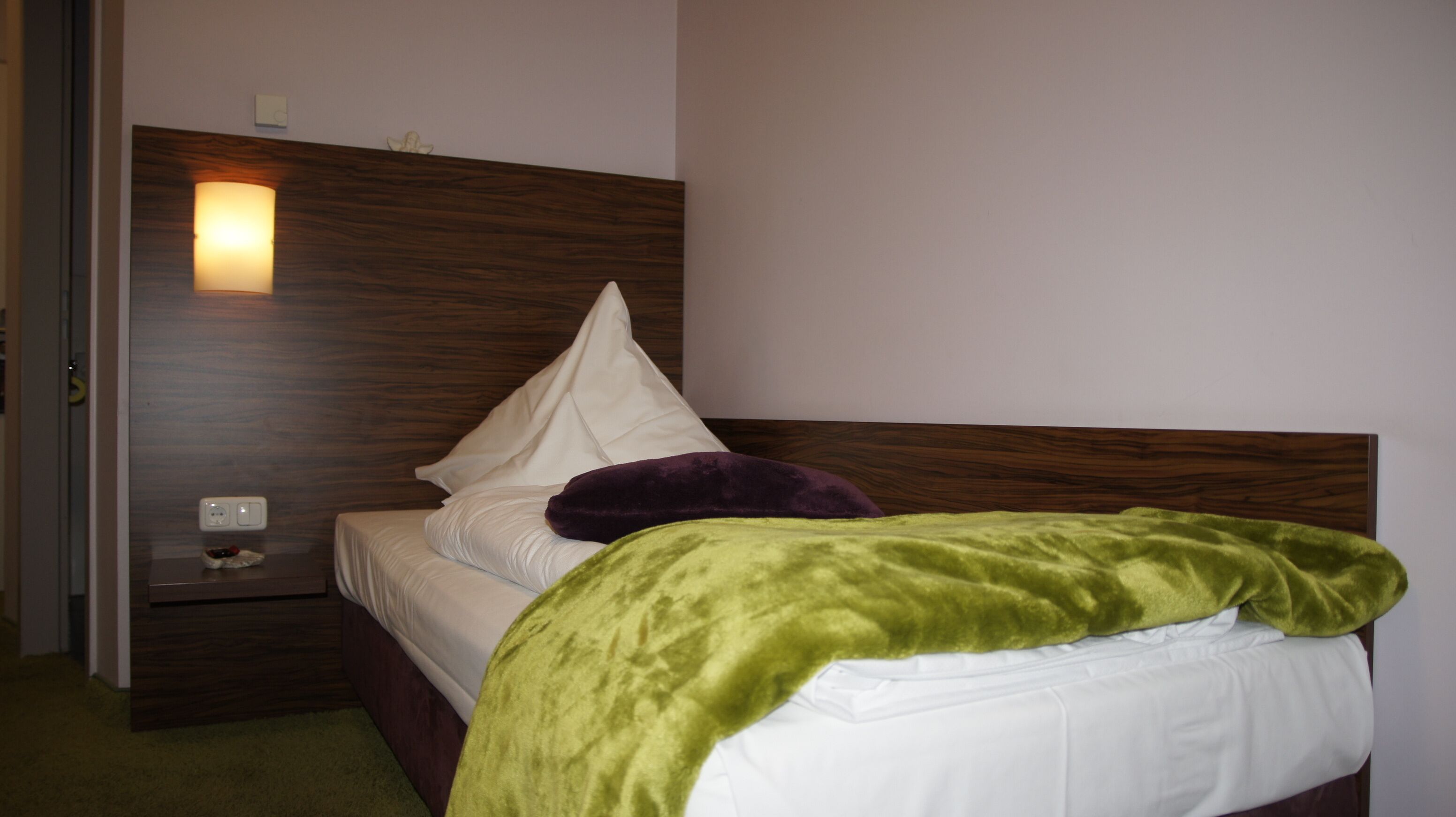 A hotel room with a wooden headboard, a white bed, a green blanket, and a purple pillow.