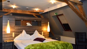 Un dormitorio con techo estilo loft, vigas de madera, una cama con ropa blanca, una manta verde y dos lámparas de noche.