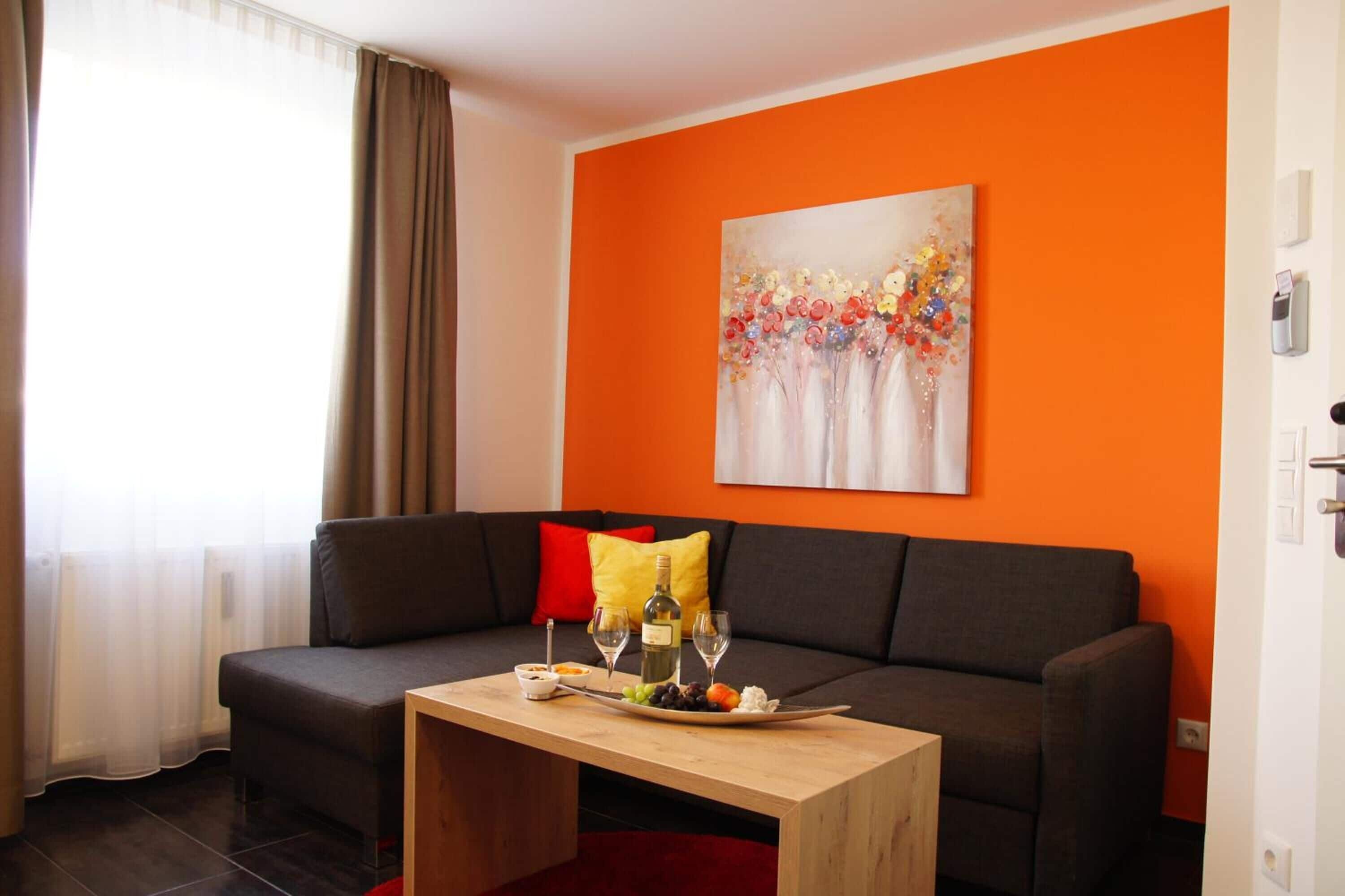A modern living room with a dark grey sofa, a wooden coffee table, and a vibrant orange accent wall.