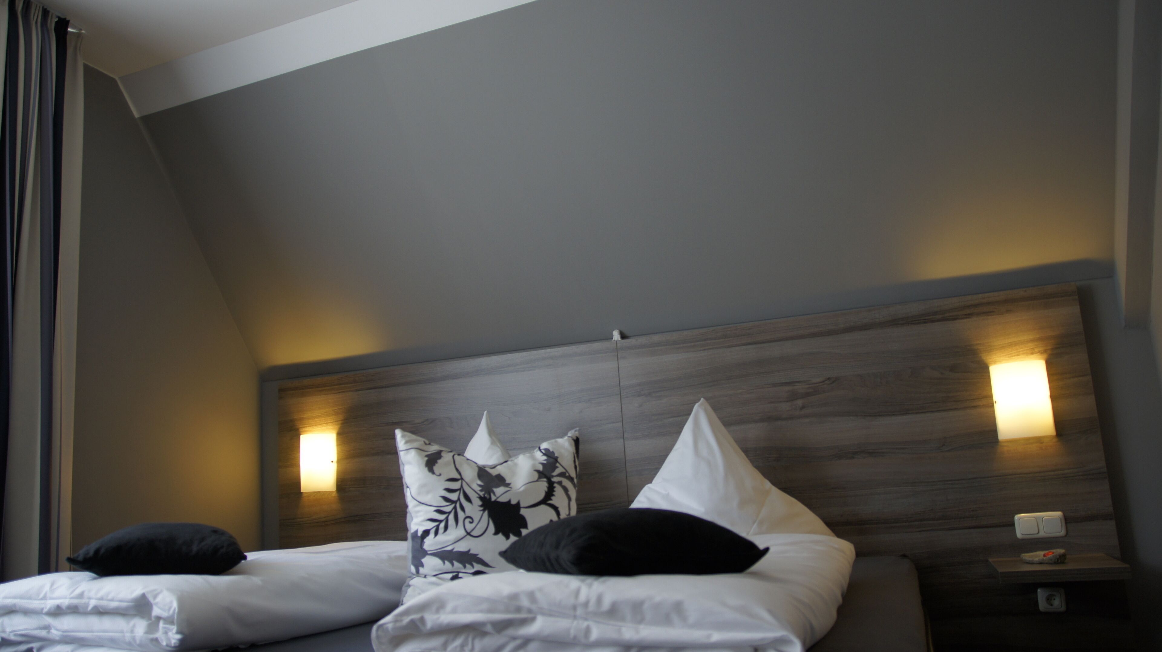 Een hotelkamer met een modern design, met een houten hoofdeinde, twee bedden met witte beddengoed en decoratieve kussens.