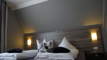 Een hotelkamer met een modern design, met een houten hoofdeinde, twee bedden met witte beddengoed en decoratieve kussens.