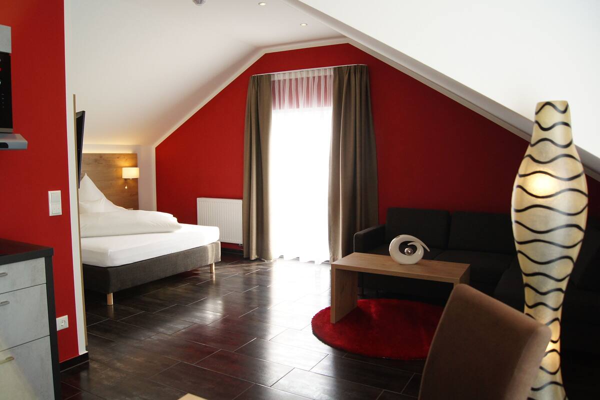 Una habitación moderna con cama, sofá, una mesita y un tapete rojo.