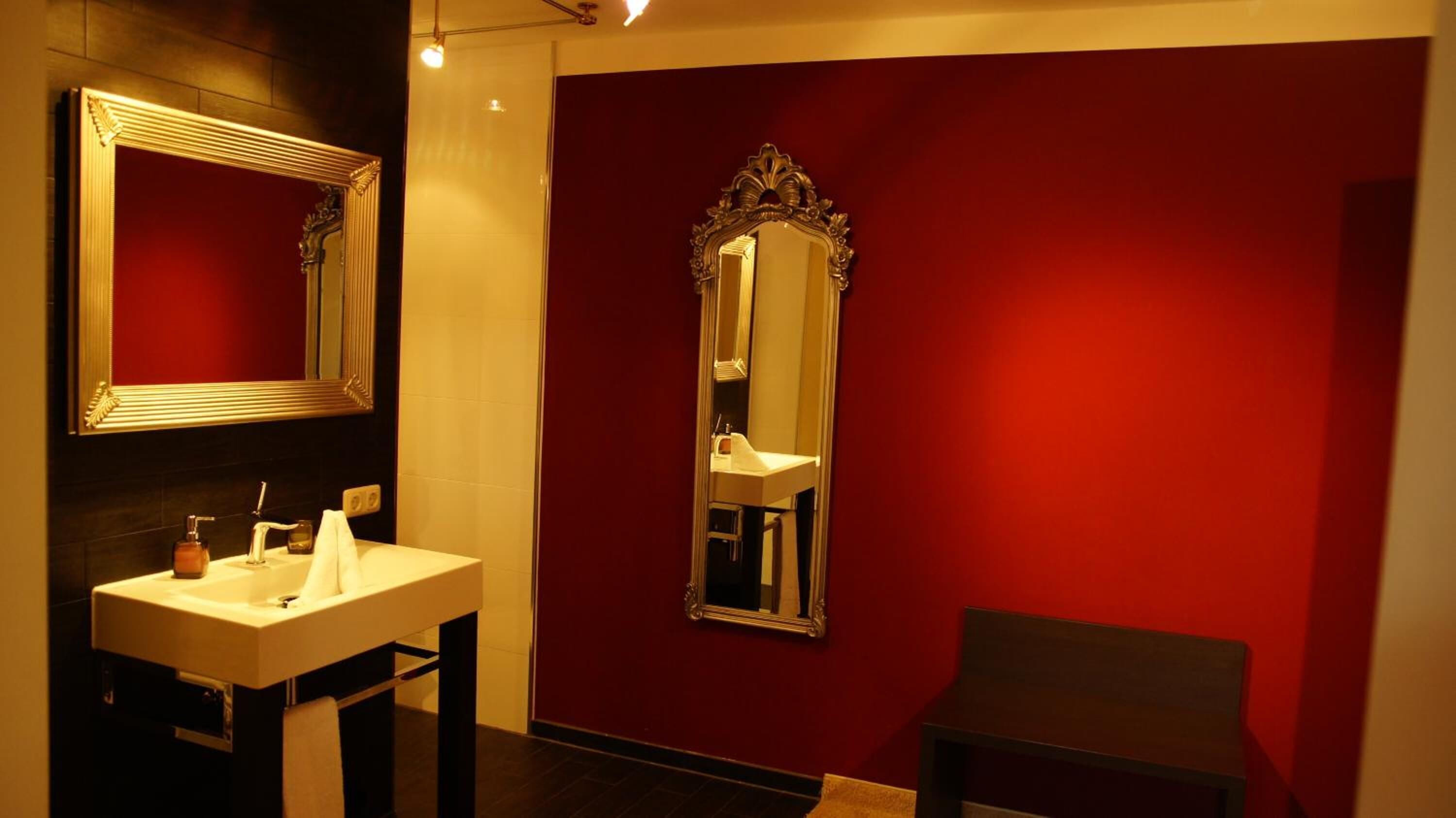 A bathroom with a white sink, two mirrors, and red walls.