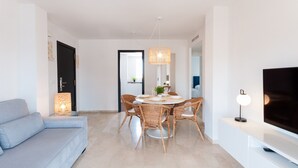Un salon moderne avec un canapé bleu clair, une table à manger avec des chaises en osier, un luminaire suspendu en osier et un téléviseur à écran plat posé sur un meuble blanc.
