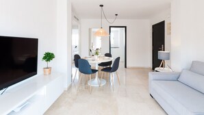 Uma sala de estar moderna com uma televisão de tela plana, um sofá e uma área de jantar com cadeiras e uma mesa.