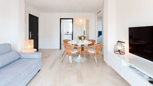 Un salon moderne comprenant un canapé, une table à manger avec des chaises, un téléviseur et une lampe.