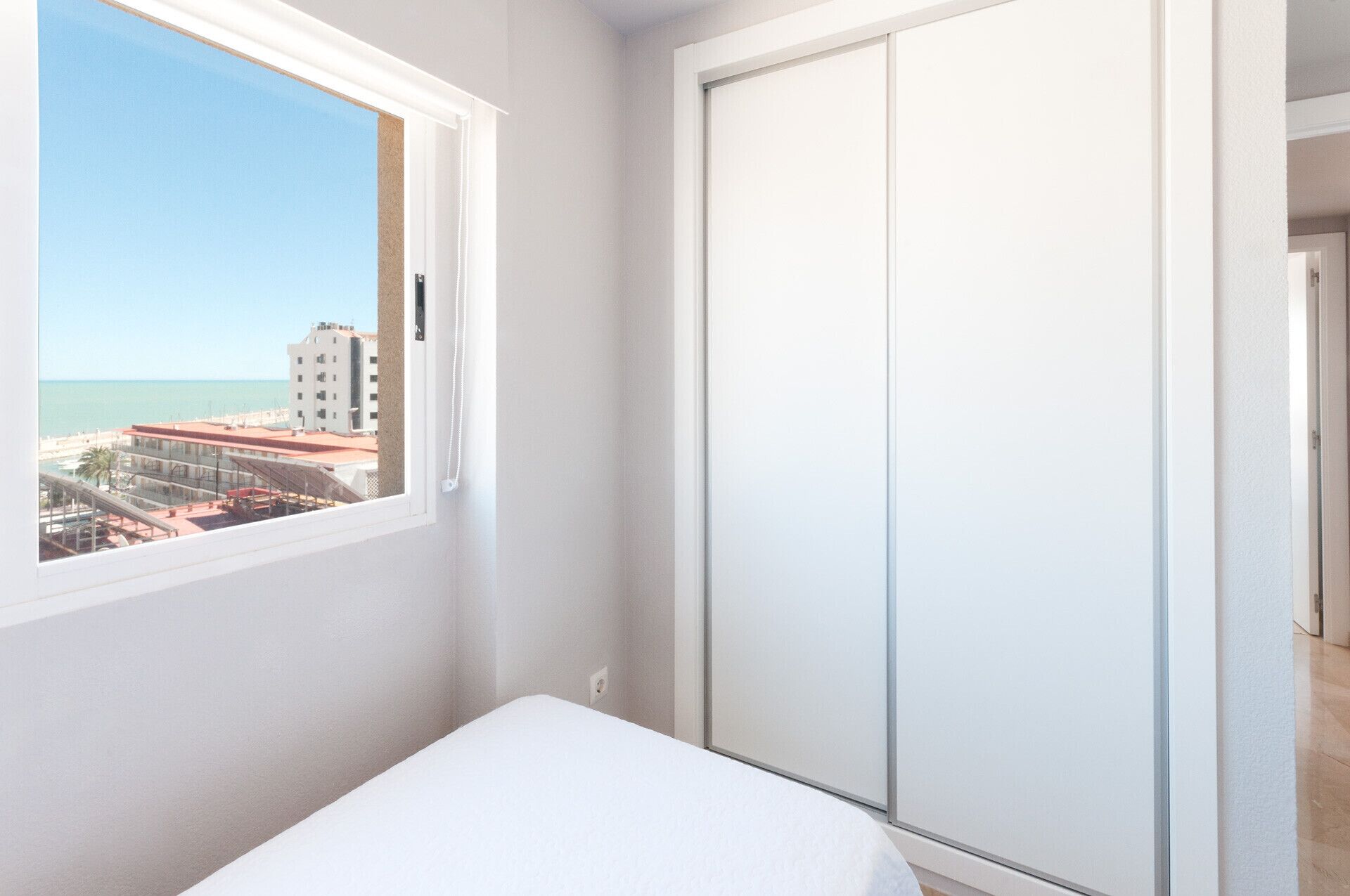 A bedroom with a window overlooking a beach and buildings.