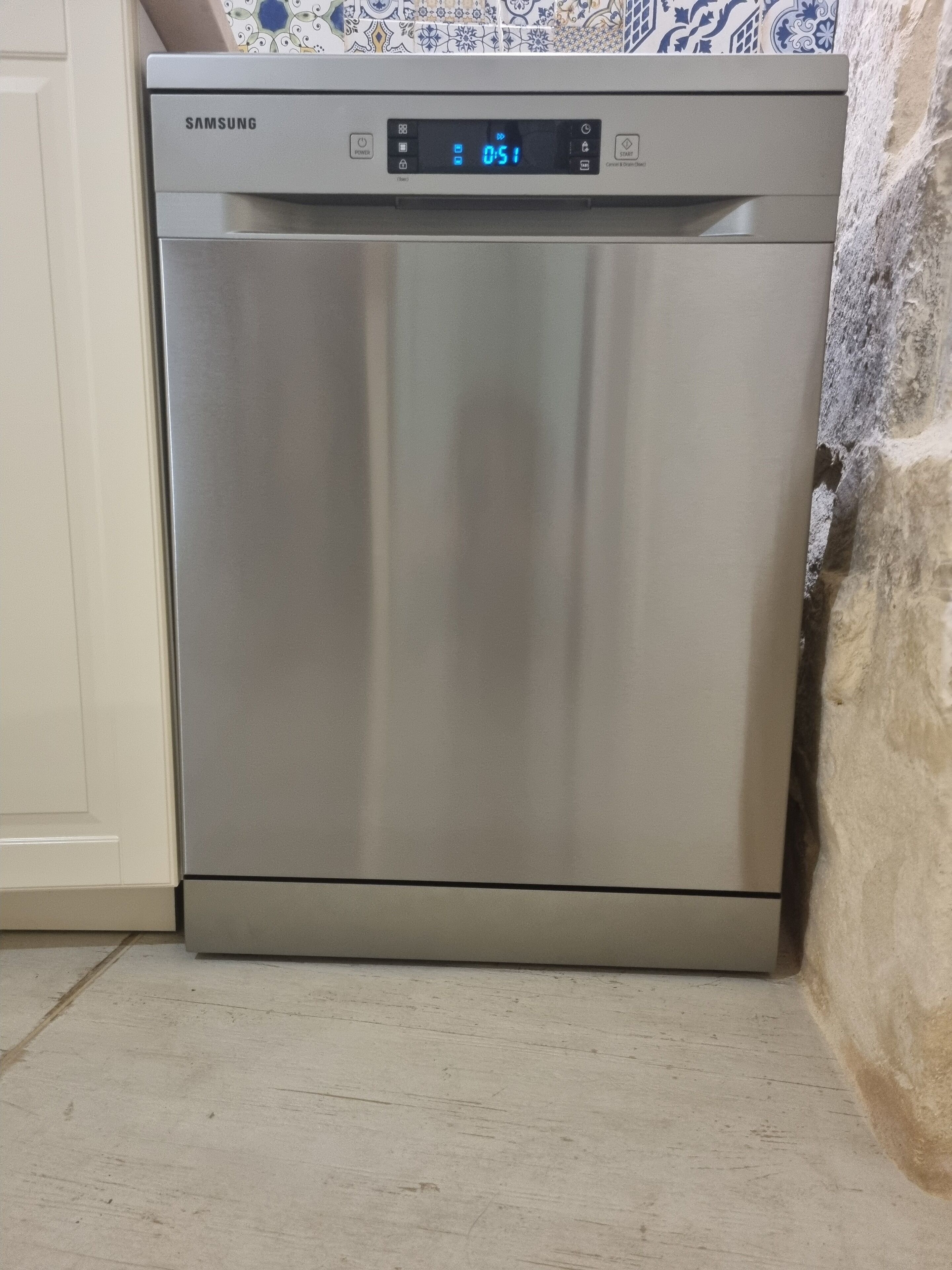 A stainless steel Samsung dishwasher in a kitchen with a tiled backsplash and a white cabinet.