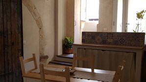 Et spiseområde med et træbord og stole, en potteplante og udsigt til et køkken med flisebeklædt bagvæg.