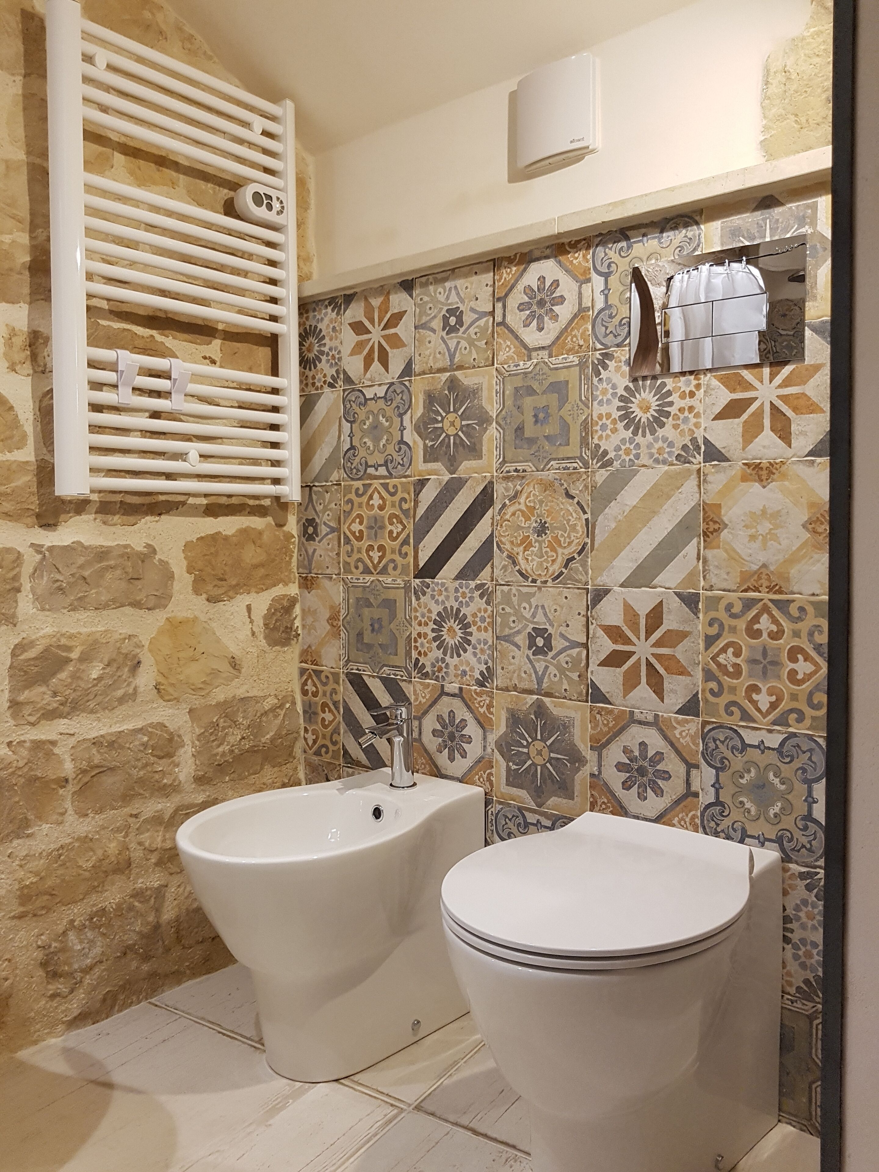 Une salle de bain avec un mur en pierre, un pare-feu en carrelage, un bidet, des toilettes et un porte-serviettes.