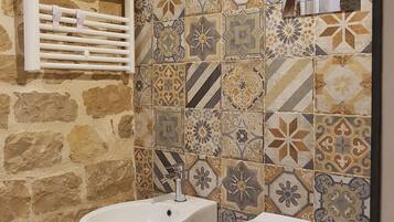 Une salle de bain avec un mur en pierre, un pare-feu en carrelage, un bidet, des toilettes et un porte-serviettes.