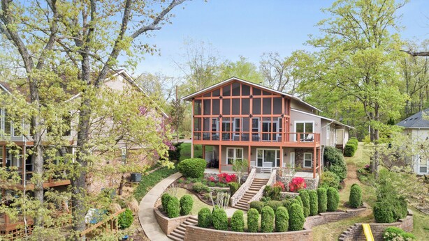 Une maison à deux étages dotée d’un balcon, entourée de jardins et d’arbres bien entretenus.