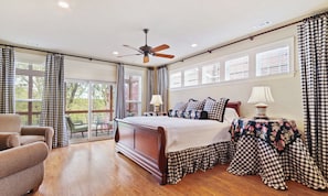 A bedroom with a large bed, a ceiling fan, a table with a lamp, and checkered curtains.