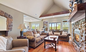 A spacious living room with a stone fireplace, wooden flooring, and multiple sofas arranged around a central coffee table.
