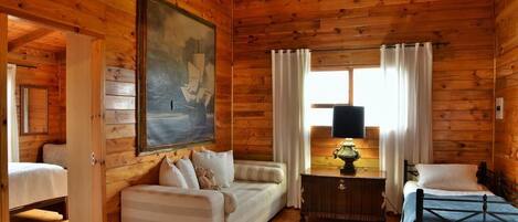 A cozy cabin with a wooden interior, a sofa, a bed, and a painting on the wall.