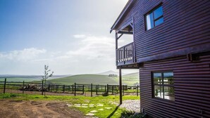 A rustic wooden building with a balcony, surrounded by a fenced pasture and rolling hills in the background. - Anna Beulah Farm (Cape Town)