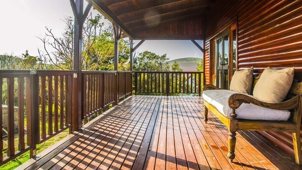 A wooden deck with a checkered floor, a wooden bench with cushions, and a view of greenery and hills in the background. - Anna Beulah Farm (Cape Town)