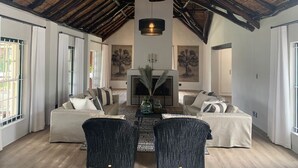 A spacious living room with a high ceiling, a fireplace, and a large window. - Anna Beulah Farm (Cape Town)