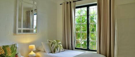 A hotel room with two beds, a window with curtains, a bedside lamp, and a mirror on the wall.