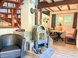 A cozy room with a stone fireplace, a dining area with a table and chairs, and a view of greenery outside.