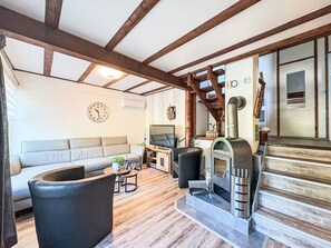 A living room with a sofa, TV, fireplace, wooden beams, and a clock.