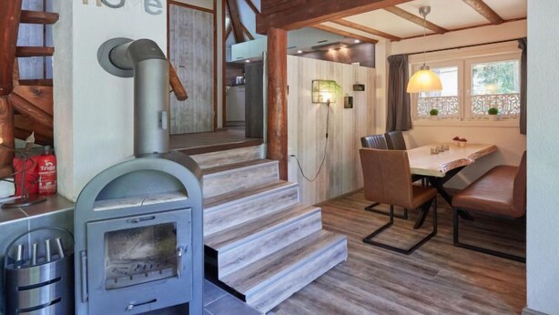 A cozy interior with a wooden staircase, a fireplace, and a dining area with a table and chairs.