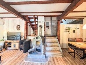 A living room with a fireplace, a TV, and a dining area with a staircase leading to another room.