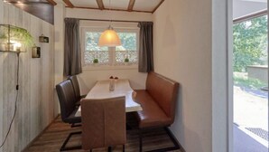 A dining area with a wooden ceiling, a table with chairs, and a window with curtains.