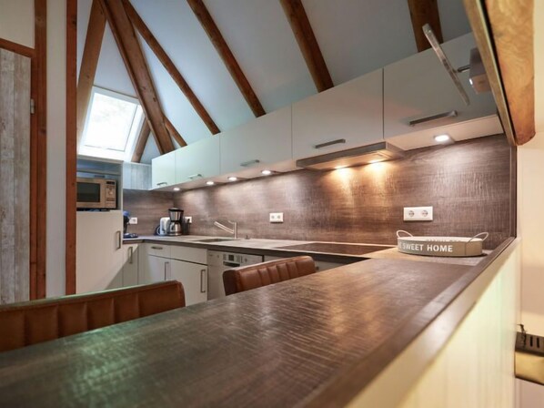 A modern kitchen with wooden beams, a large island, and a view of the outdoors. - Am Sternberg 50 by Interhome (Frankenau)
