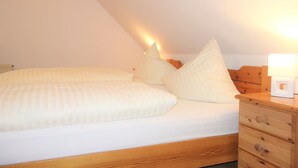 Ein Schlafzimmer mit einem hölzernen Bett, weißer Bettwäsche und einem Nachttisch mit Lampe.