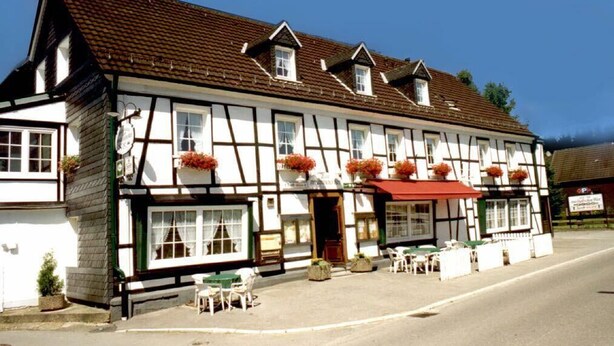 Ein traditionelles Fachwerkhäuschen mit roter Markise und Außenbestuhlung.