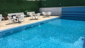 A swimming pool with clear blue water, surrounded by white outdoor furniture and a green hedge. - Otel 1919 (Atakum)
