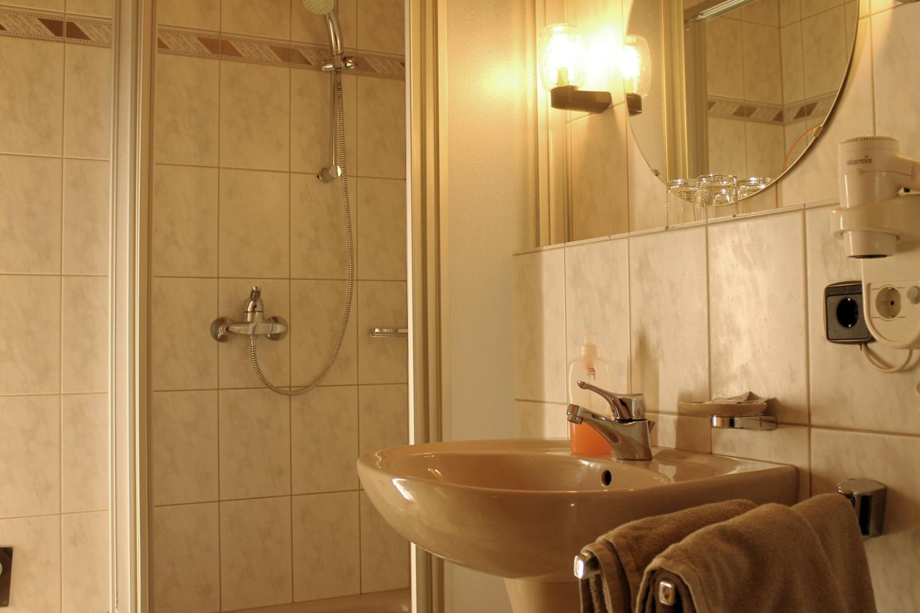 Un baño con un lavamanos color beige, un cabezal de ducha de mano, un espejo y un perchero para toallas.