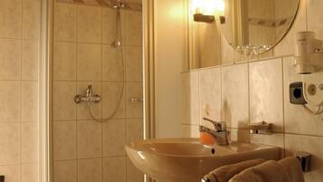 Un baño con un lavamanos color beige, un cabezal de ducha de mano, un espejo y un perchero para toallas.
