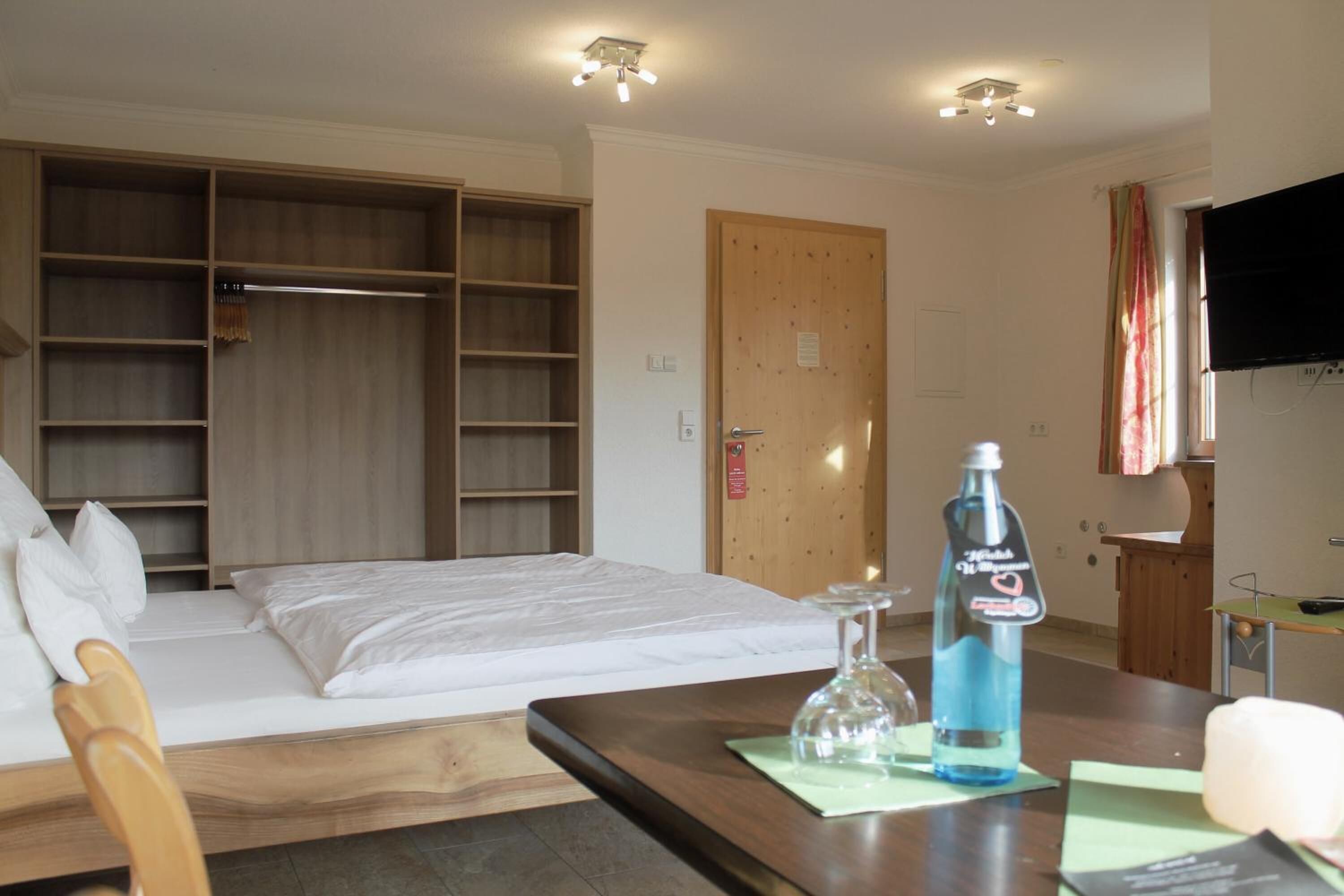 Habitación de hotel con cama, armario de madera, televisor y una botella de agua sobre la mesa.