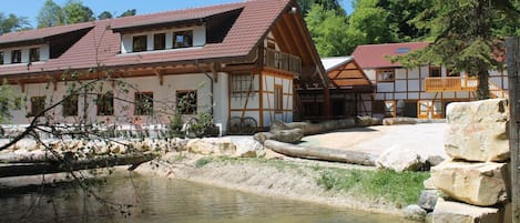 A traditional building with a sloped roof and wooden beams, adjacent to a calm water body with a stone barrier.