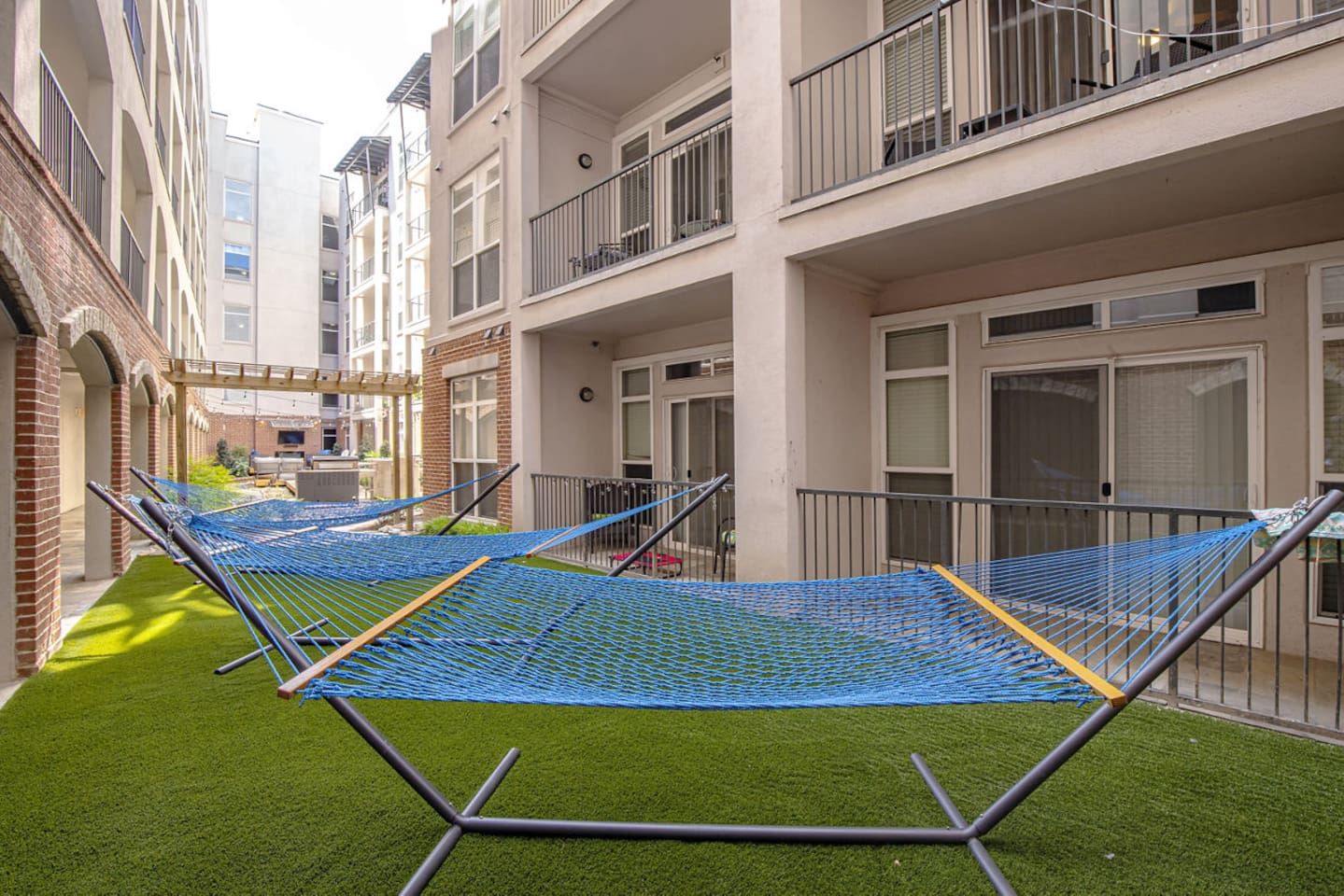 Een binnentuin met meerdere blauwe hangmatten op kunstgras, omringd door meerlaagsgebouwen met balkons.