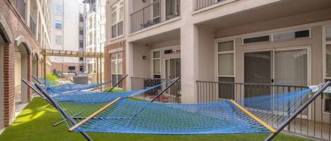 A courtyard with multiple blue hammocks on artificial grass, surrounded by multi-story buildings with balconies.