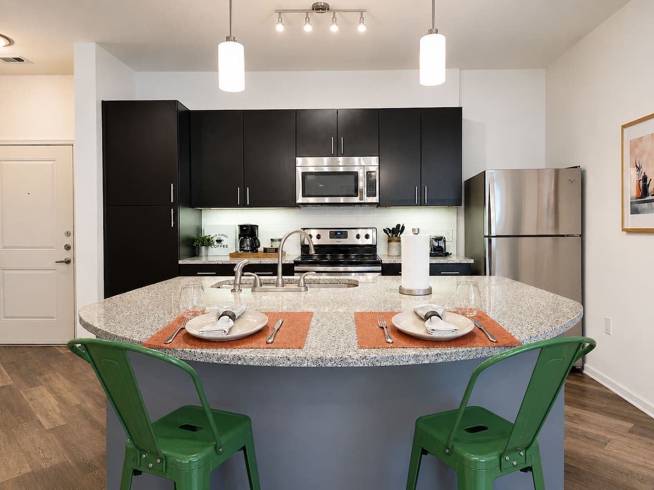A modern kitchen with dark cabinets, stainless steel appliances, and a central island with two chairs.