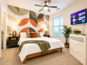 Un dormitorio con cama, mesitas de noche, televisor y una pared con arte abstracto.