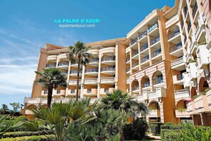 Experience the elegant architecture of LA PALME D'AZUR, featuring arched windows and a central courtyard surrounded by lush landscaping.