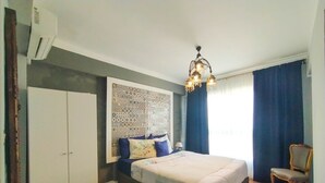 Een slaapkamer met een groot bed, een kledingkast, een bekledingspaneel met patroon, een kroonluchter en een stoel.
